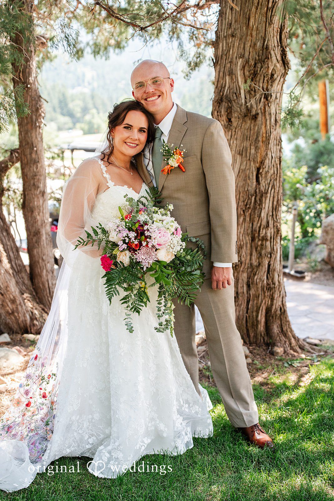 Mckenna + Ryan A bride holding a vibrant bouquet while standing next to her groom near a large tree.