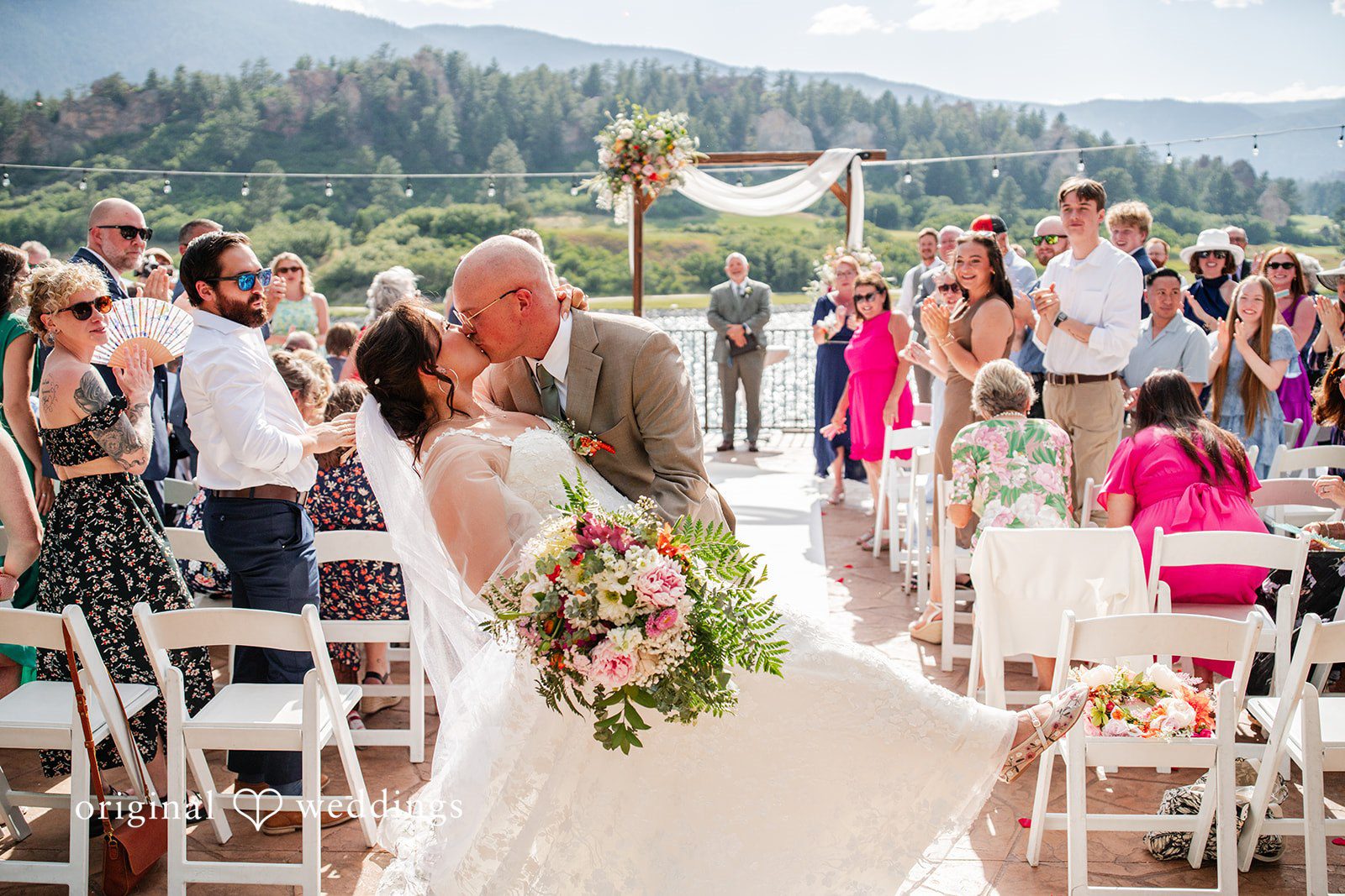 Mckenna + Ryan A groom and bride carrying a bouquet walking down the aisle and kissing each other while guests applauds..