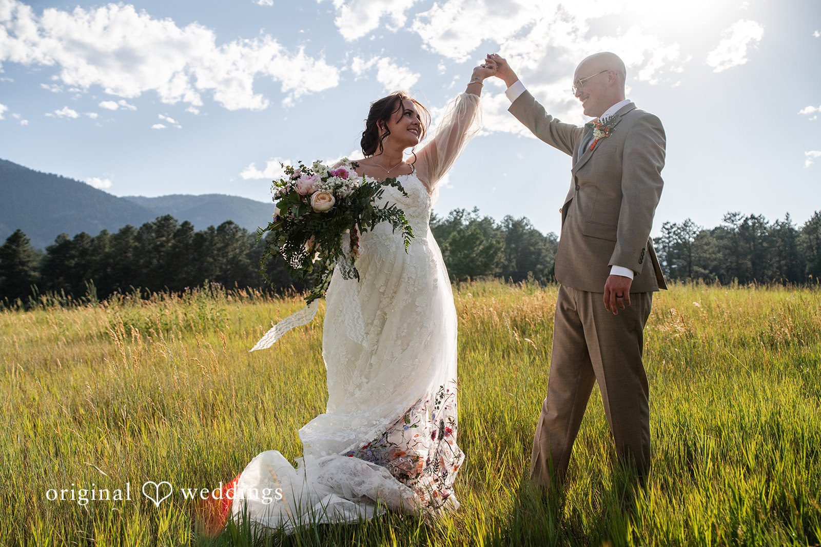 Mckenna + Ryan A bride and groom playfully posing and raising their hands in a grassy field.