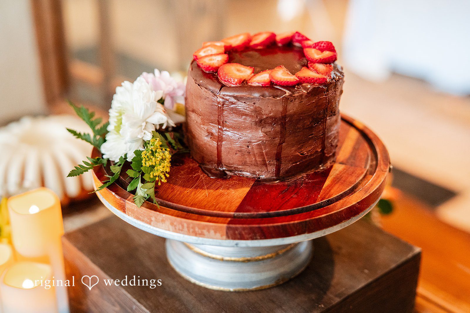 Mckenna + Ryan A small wedding cake topped with strawberries and berries on a wooden stand.
