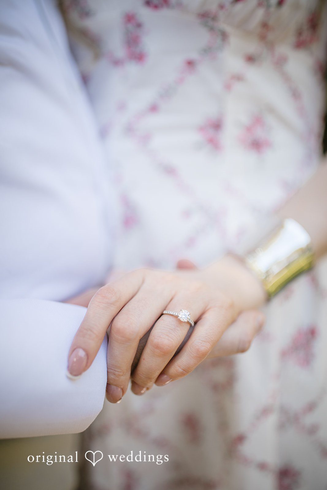 Close-up of a bride hand with a ring resting on groom arm.