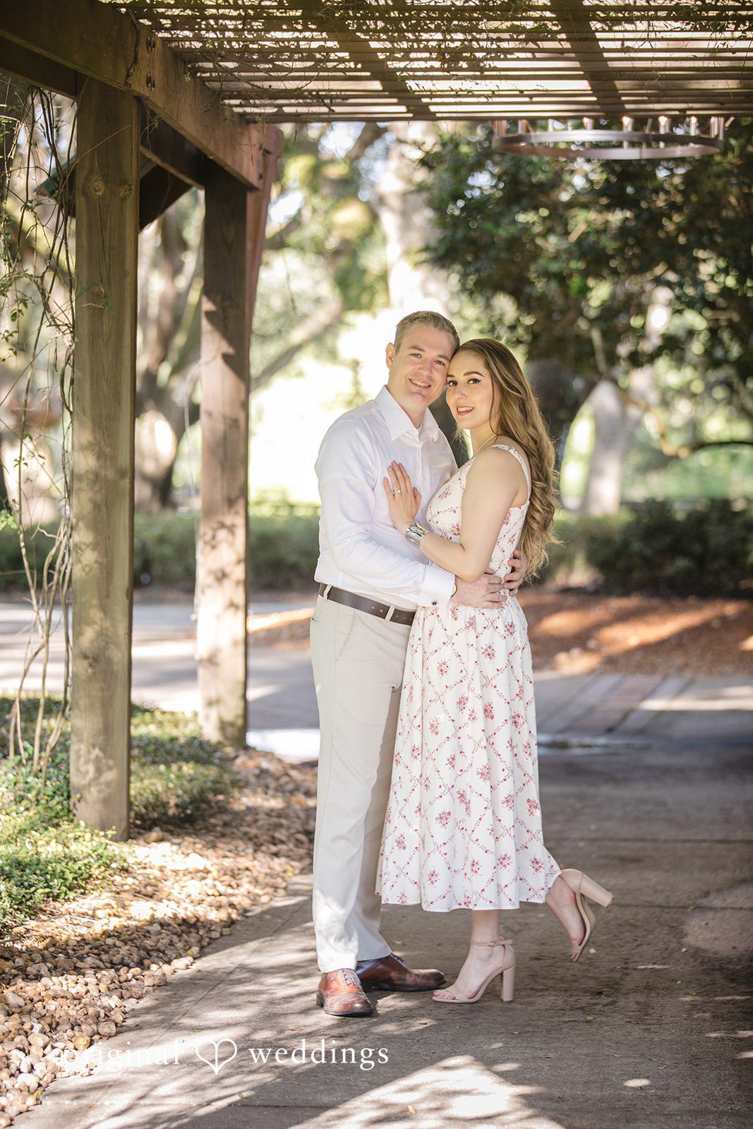 Couple embracing and smiling under a canopy of trees.