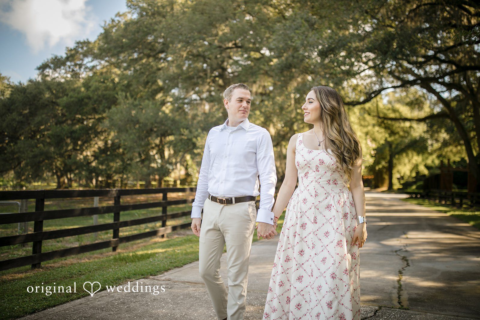 Couple walking side-by-side along a white farm fence.