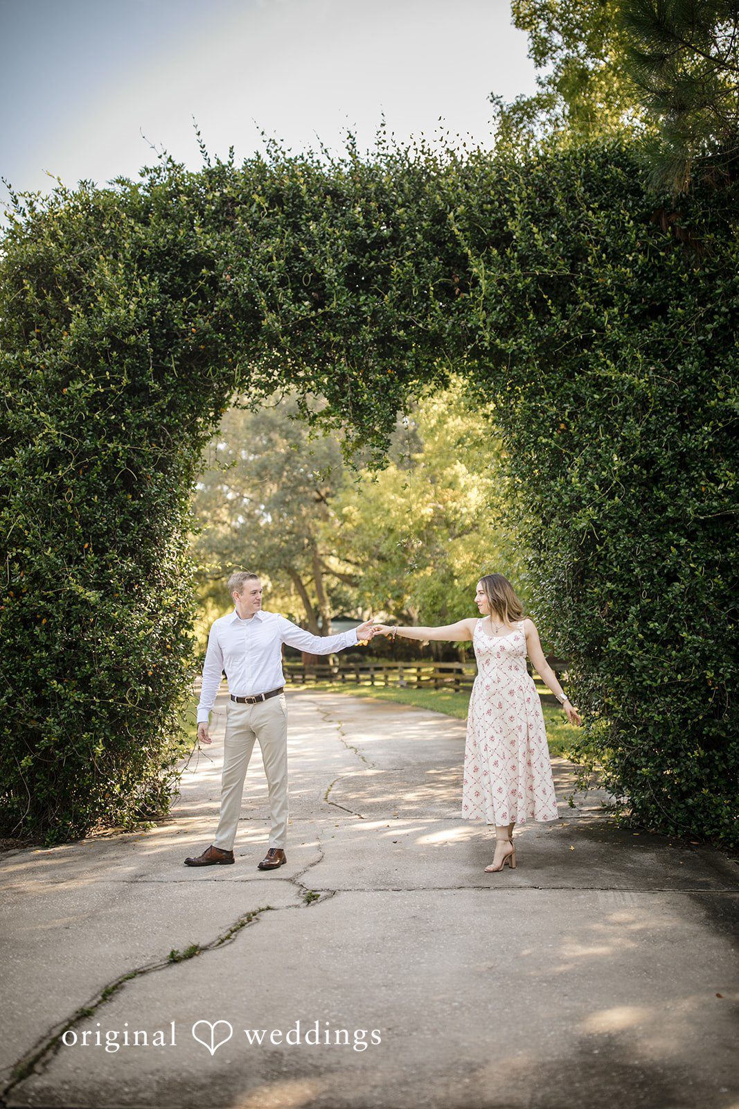 Wide shot of a man and woman holding hands near a tall hedge.