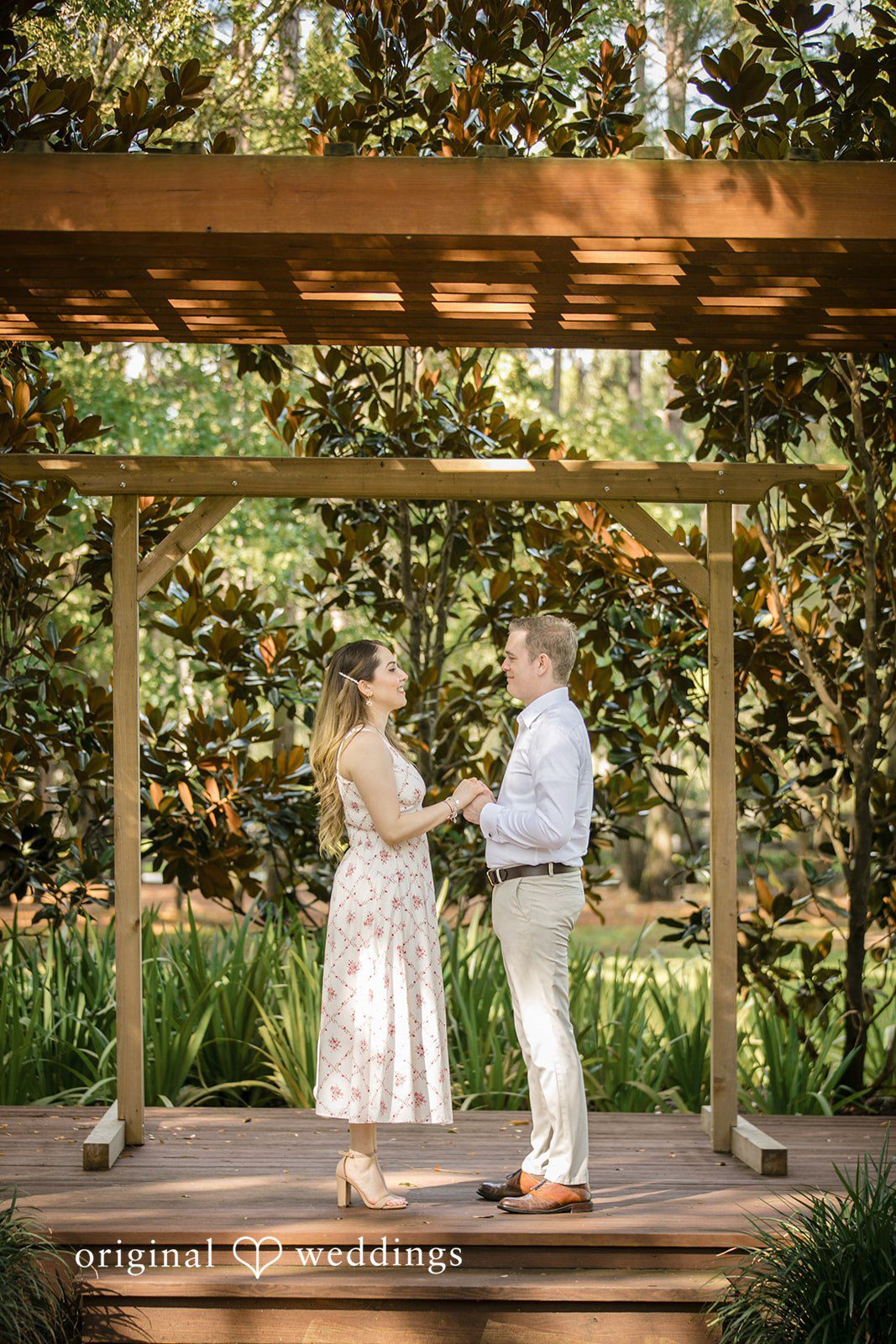 Couple holding hands while standing under a wooden pergola.