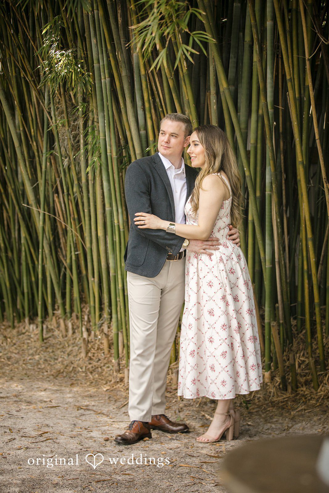 Couple standing close together and smiling on a paved path.