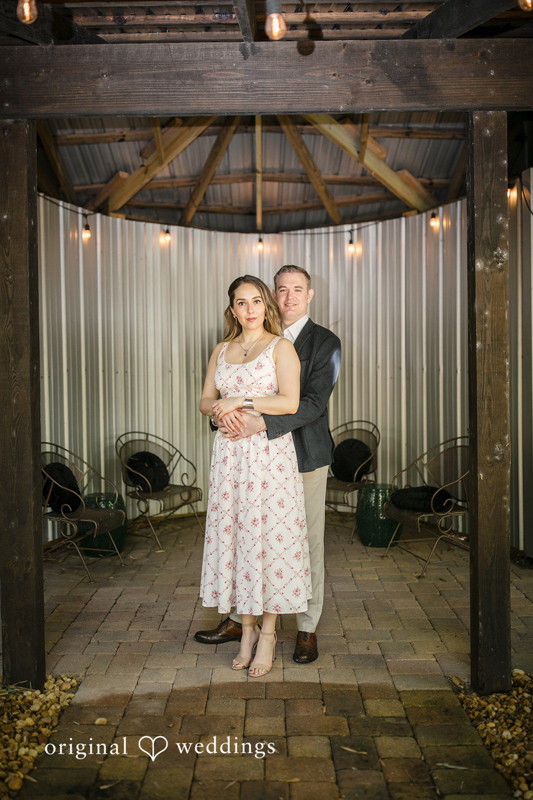 Couple standing together underneath a rustic wooden structure.