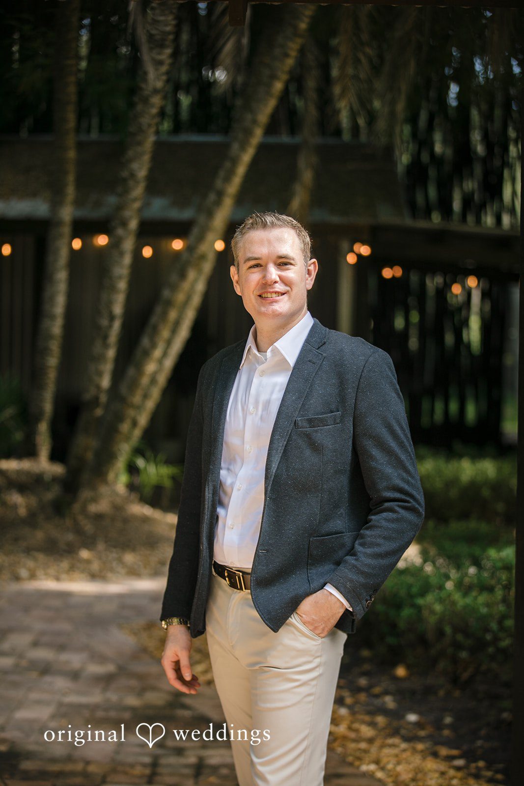 Man wearing a blazer and smiling while standing on a path.