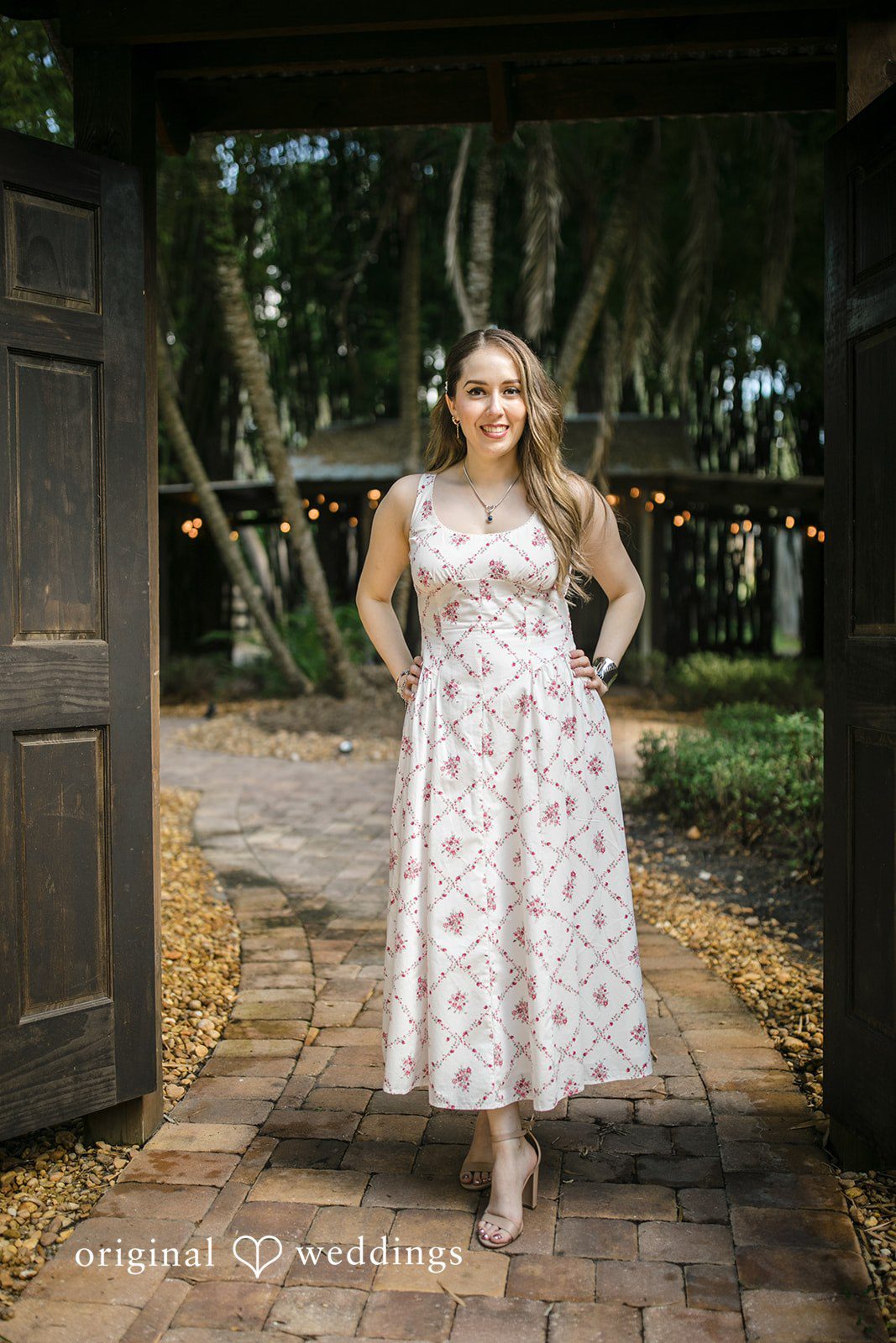 Bride in a patterned midi dress posing on a brick pathway.