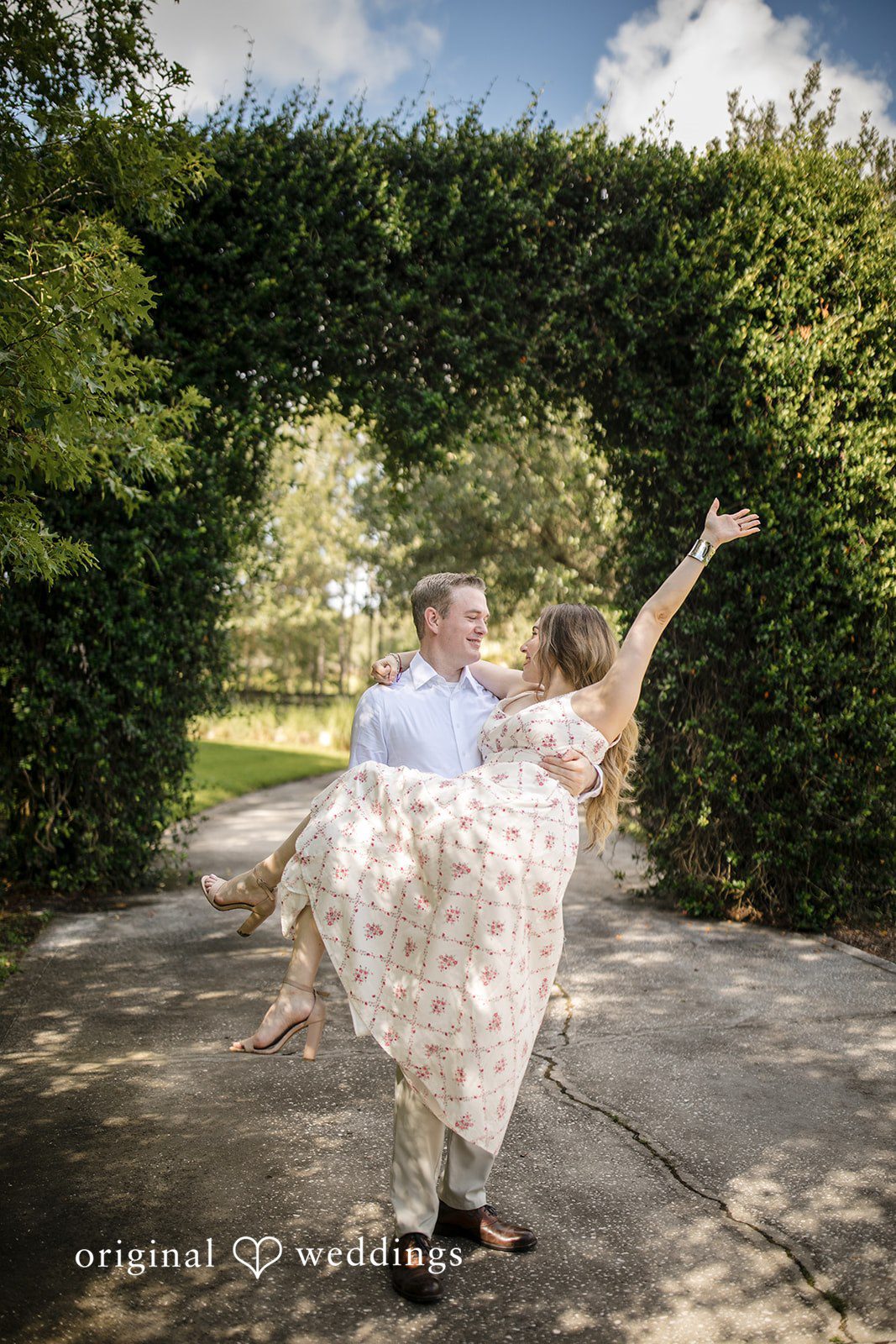 Man spinning a woman around on a pathway near a green hedge.
