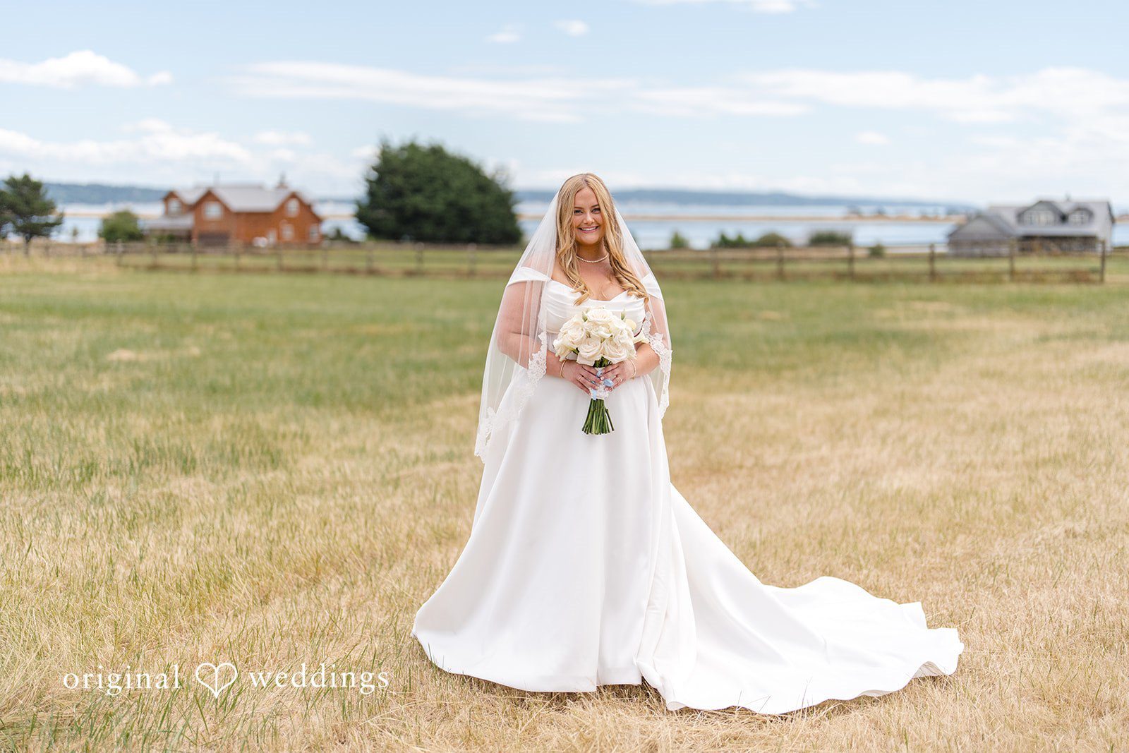 Madelyn + Connor A bride wearing a long veil and gown while standing alone in a vast field.