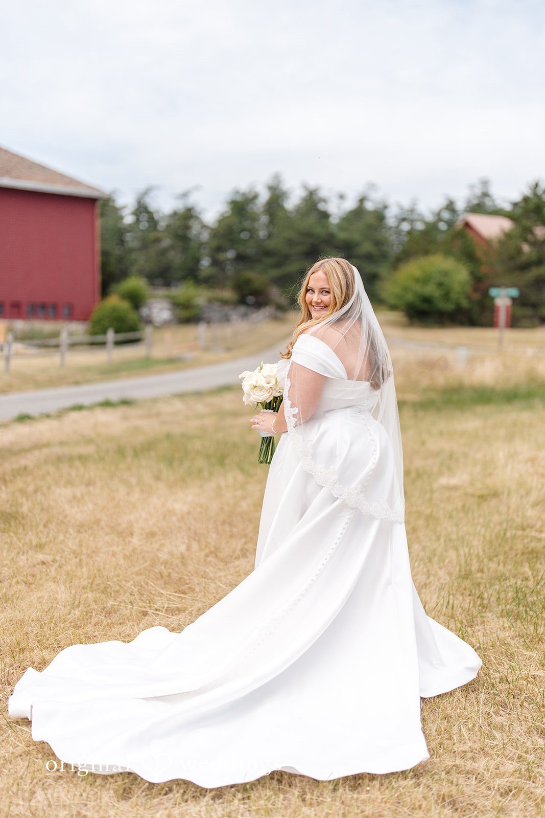 Madelyn + Connor A bride looking over her shoulder while walking through an open grassy field.