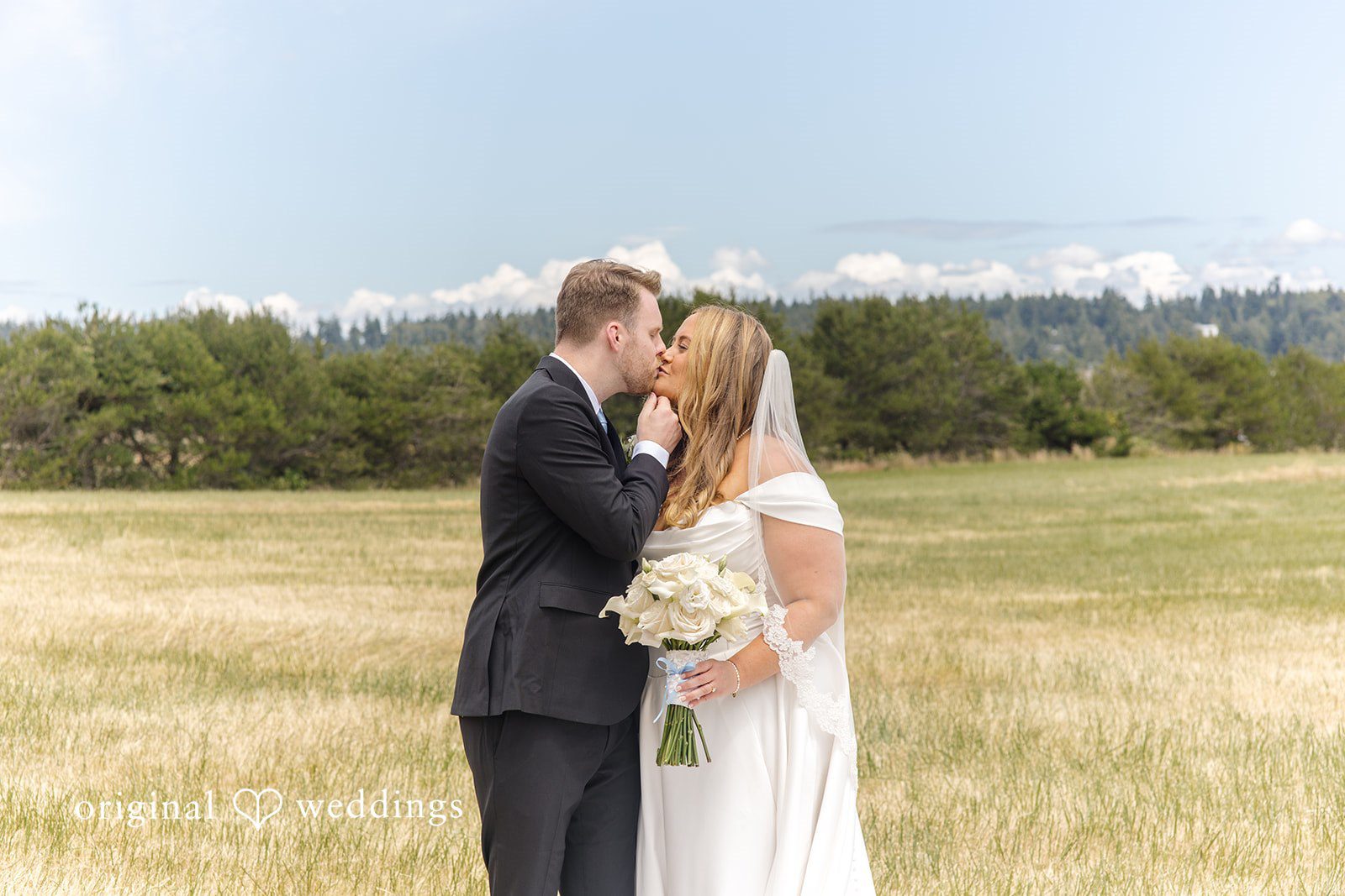 Madelyn + Connor A bride and groom kissing in an open field under a blue sky.