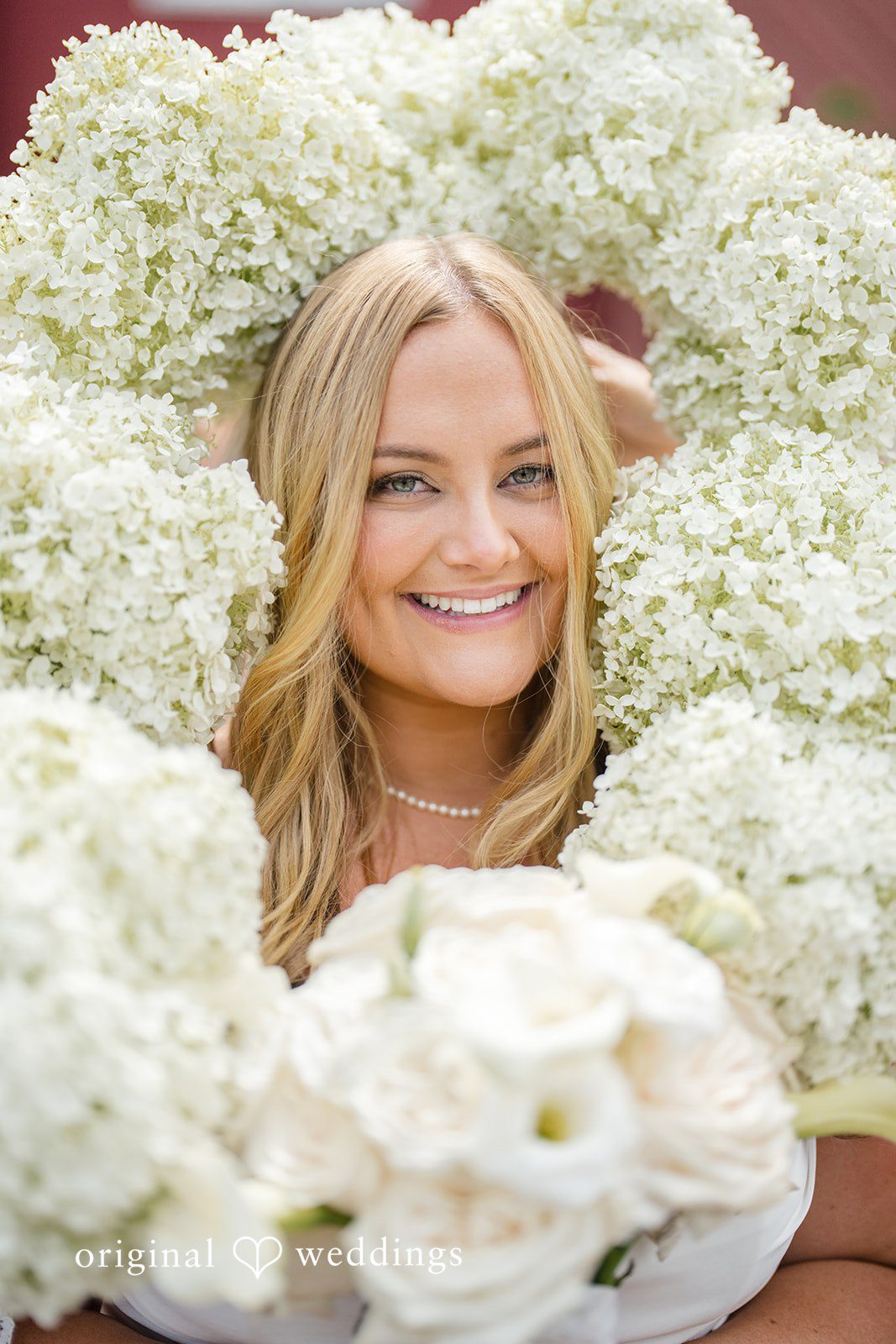 Madelyn + Connor A close-up portrait of a bride peeking through a large wreath of white flowers.