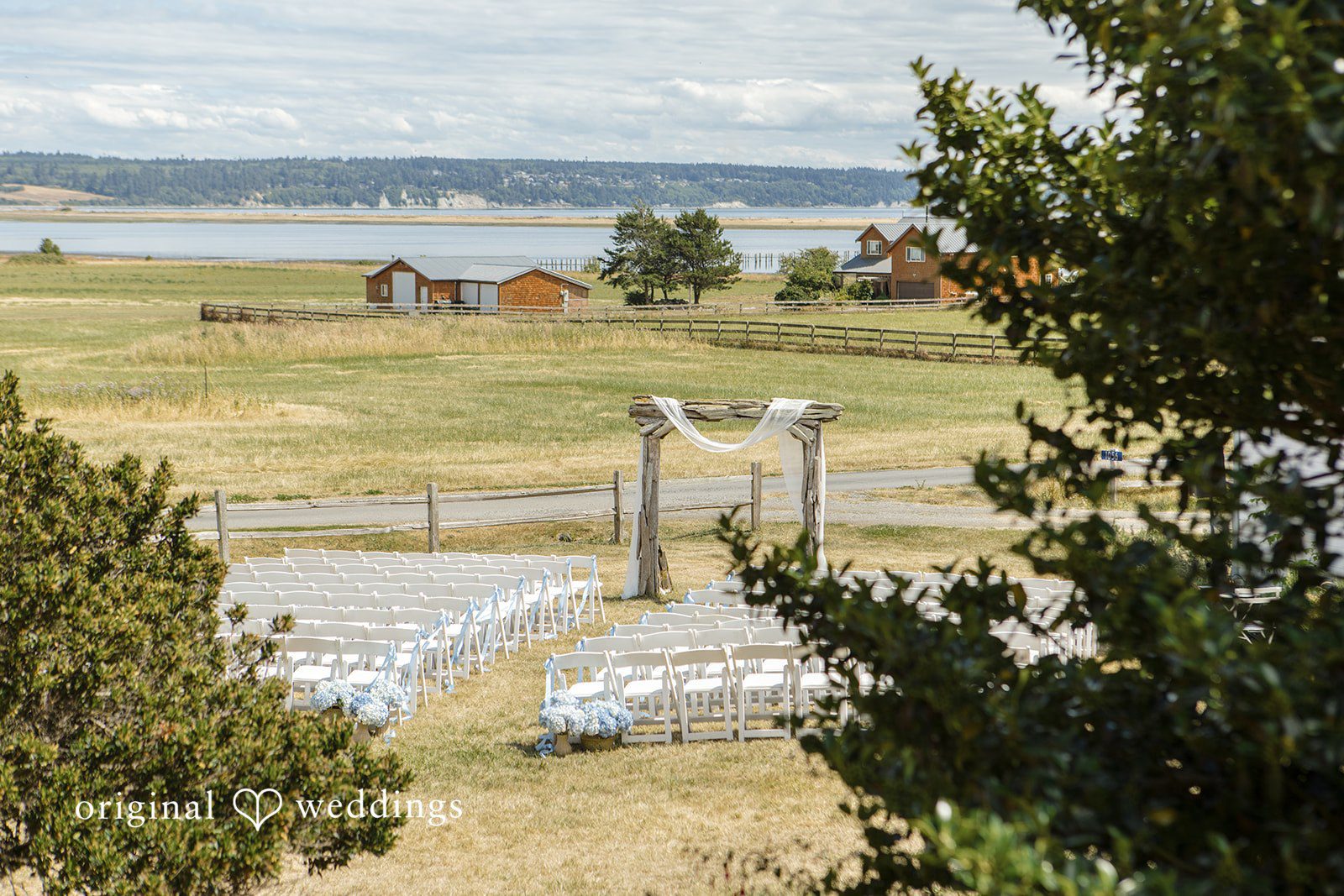 Madelyn + Connor A view looking down toward an empty wedding ceremony venue arranged in a grassy field.