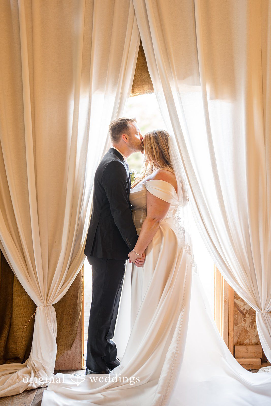 Madelyn + Connor A bride and groom holding hands between draped sheer white curtains.
