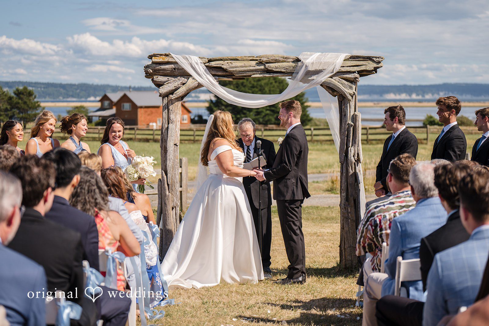 Madelyn + Connor A bride and groom standing together beneath a rustic wooden ceremony arch.