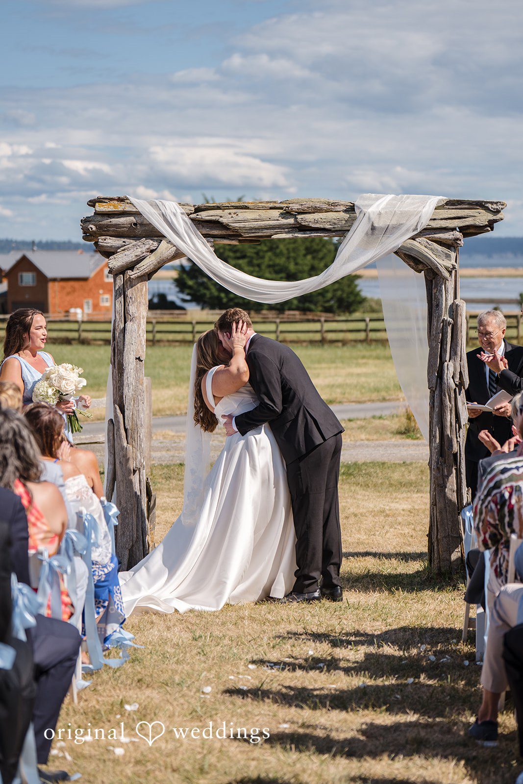 Madelyn + Connor A bride and groom sharing a kiss underneath a wooden arch at the altar.