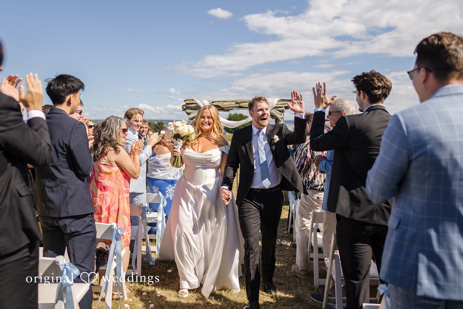 Madelyn + Connor Wedding guests standing and cheering along the aisle as a ceremony .