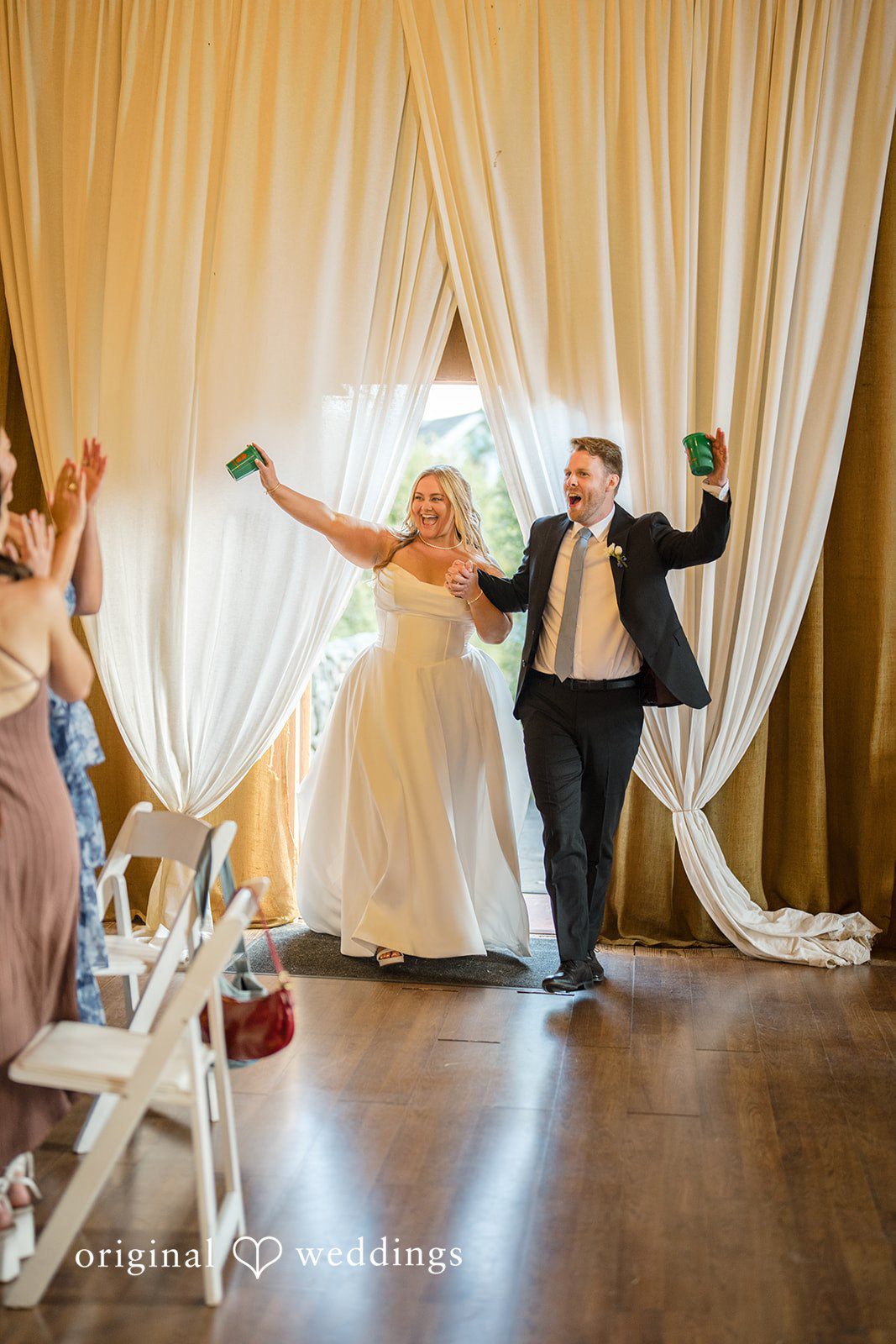 Madelyn + Connor A bride and groom making a grand entrance into a reception space with raised arms.