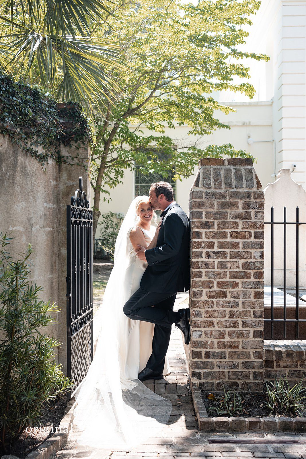 Maggie + Taylor A bride and groom share an embrace next to a historic brick structure.