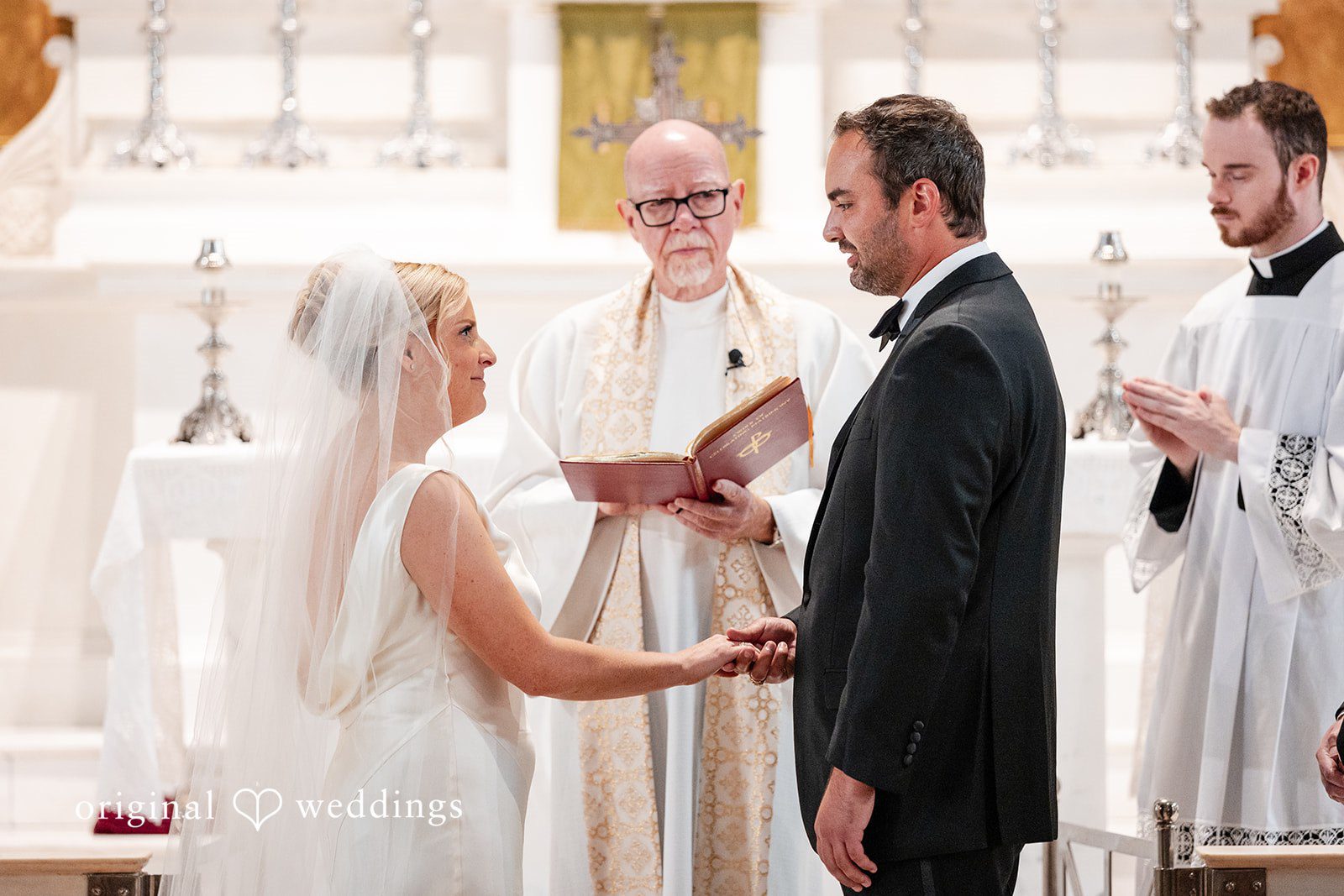 Maggie + Taylor A bride and groom exchange vows in front of an officiant during their church ceremony.