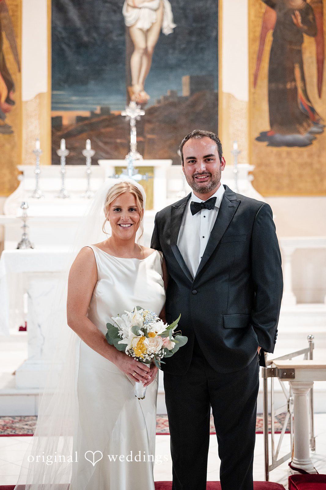 Maggie + Taylor A bride and groom pose together smiling inside a church sanctuary.