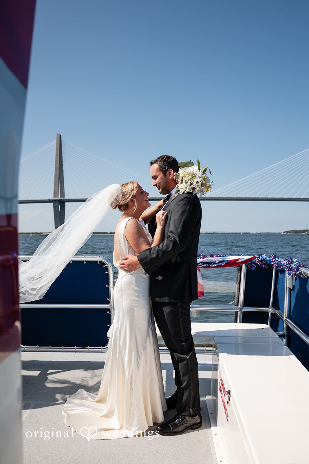 Maggie + Taylor A bride and groom stand close together on a boat overlooking the water.