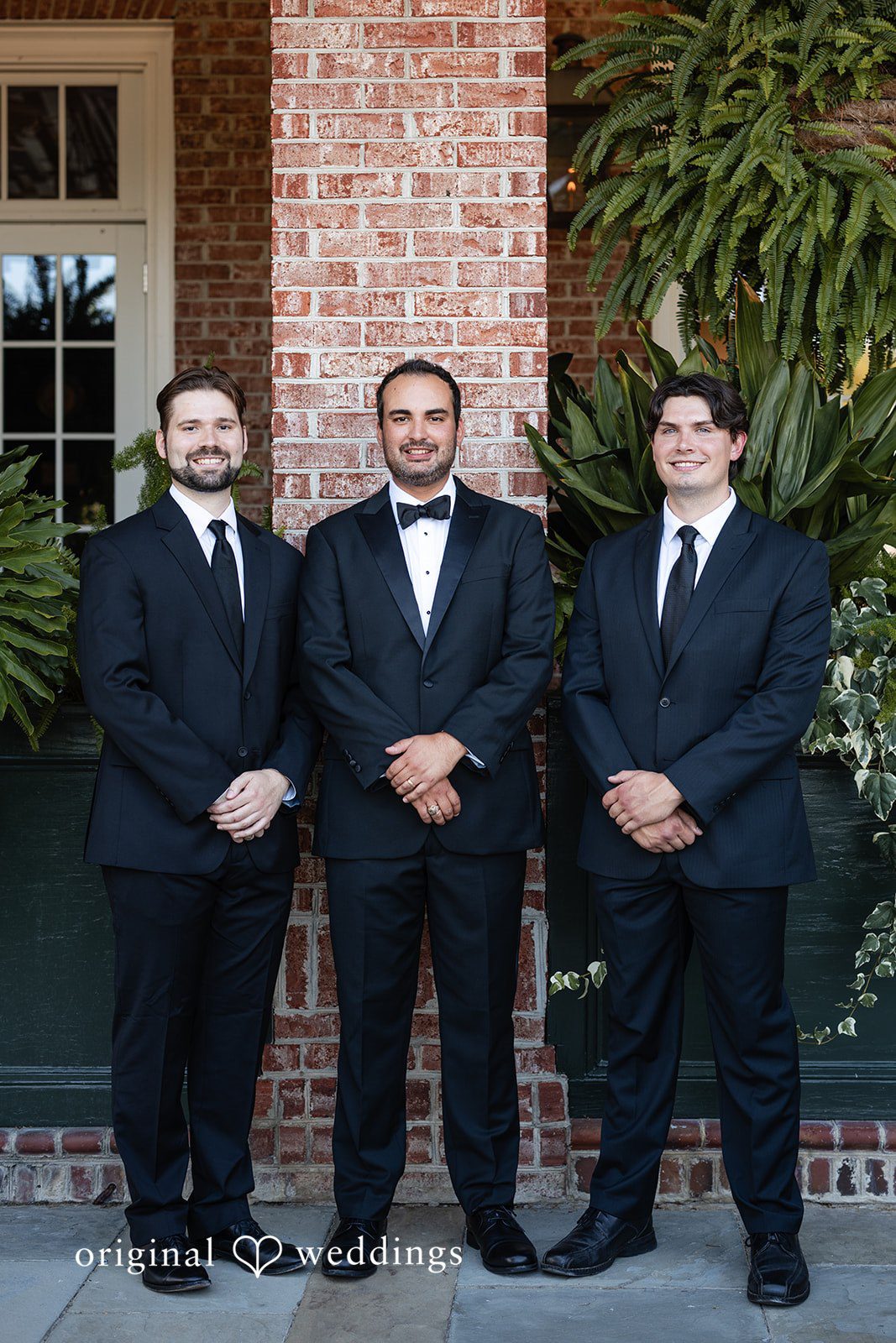 Maggie + Taylor Three groomsmen dressed in sharp black tuxedos stand side-by-side.