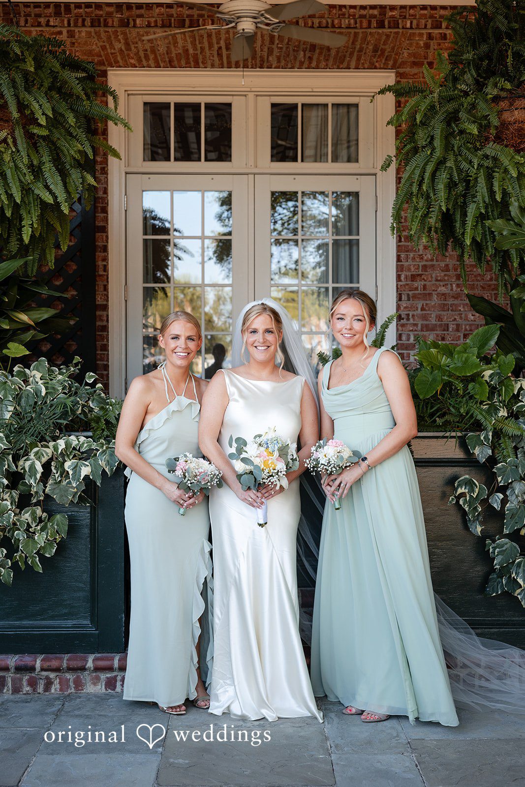 Maggie + Taylor Three bridesmaids dressed in matching sage green gowns hold floral bouquets.