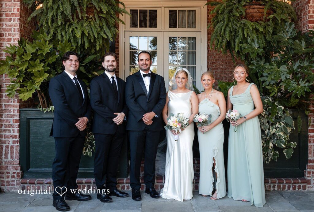 Maggie + Taylor A wedding party consisting of groomsmen and bridesmaids poses outside a building at Daniel Island Yacht Club by Charleston Wedding Photographers from Original Wedding.