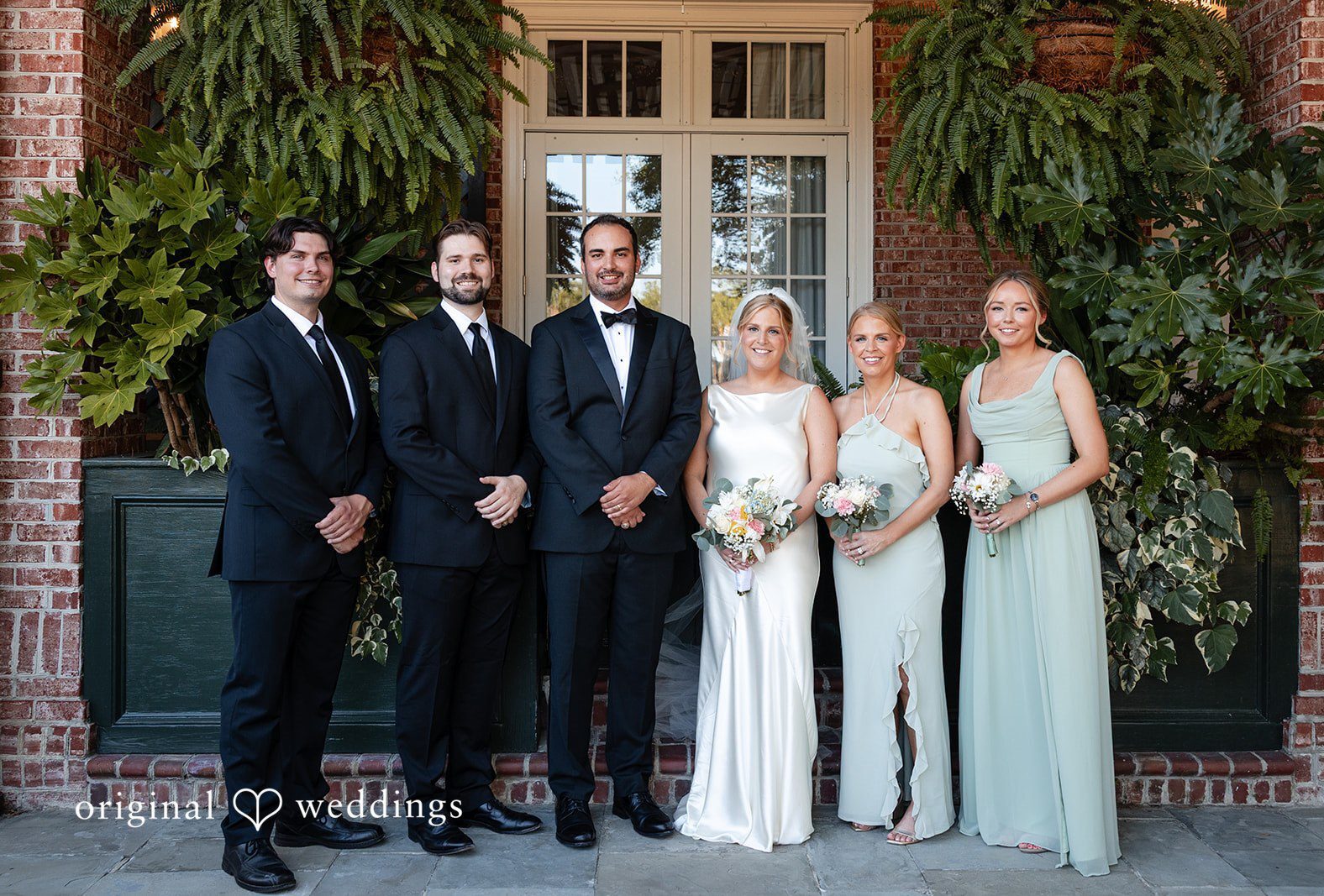 A wedding party consisting of groomsmen and bridesmaids poses outside a building at Daniel Island Yacht Club by Charleston Wedding Photographers from Original Wedding.