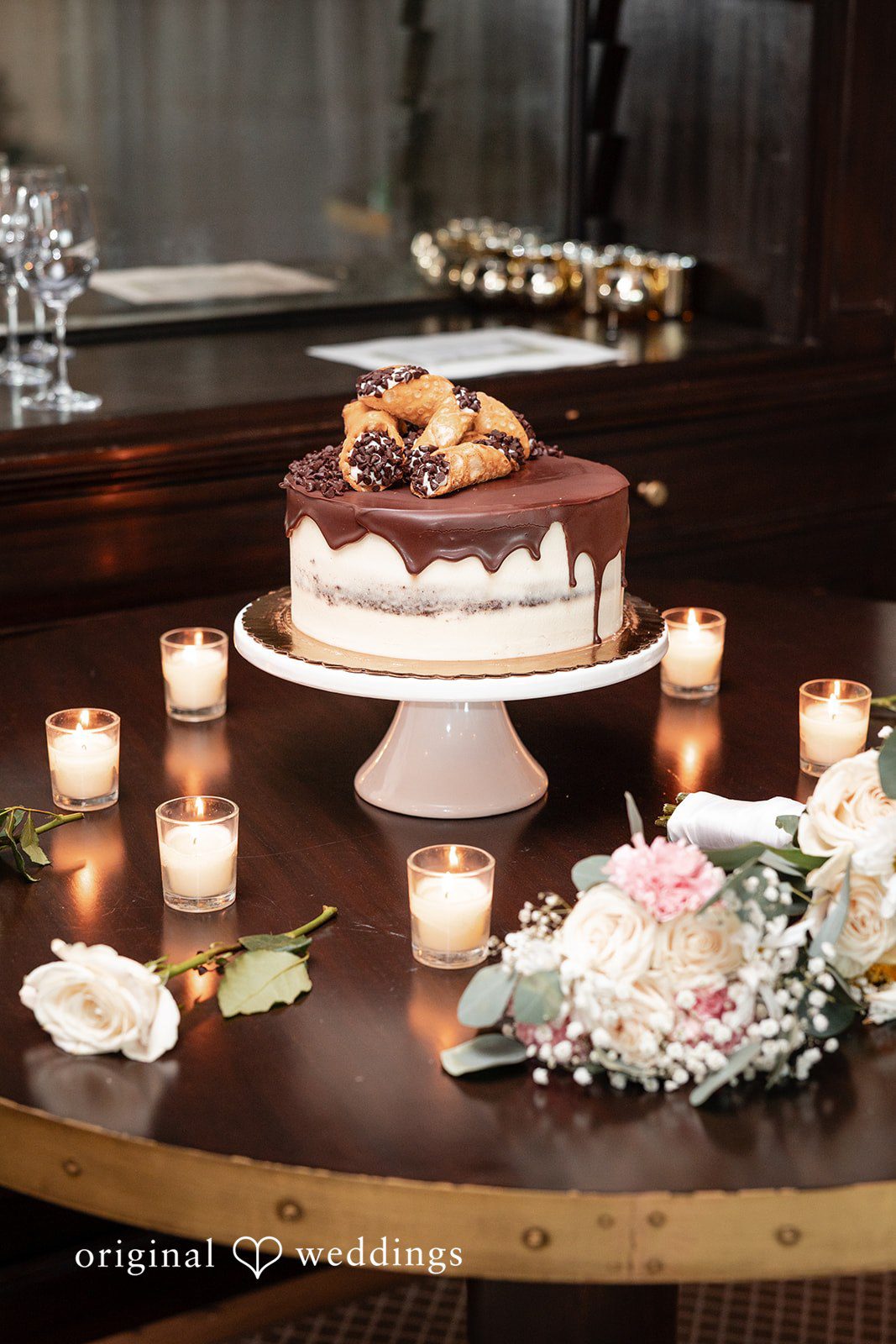 Maggie + Taylor A multi-tiered wedding cake displayed on a table illuminated by small candles.