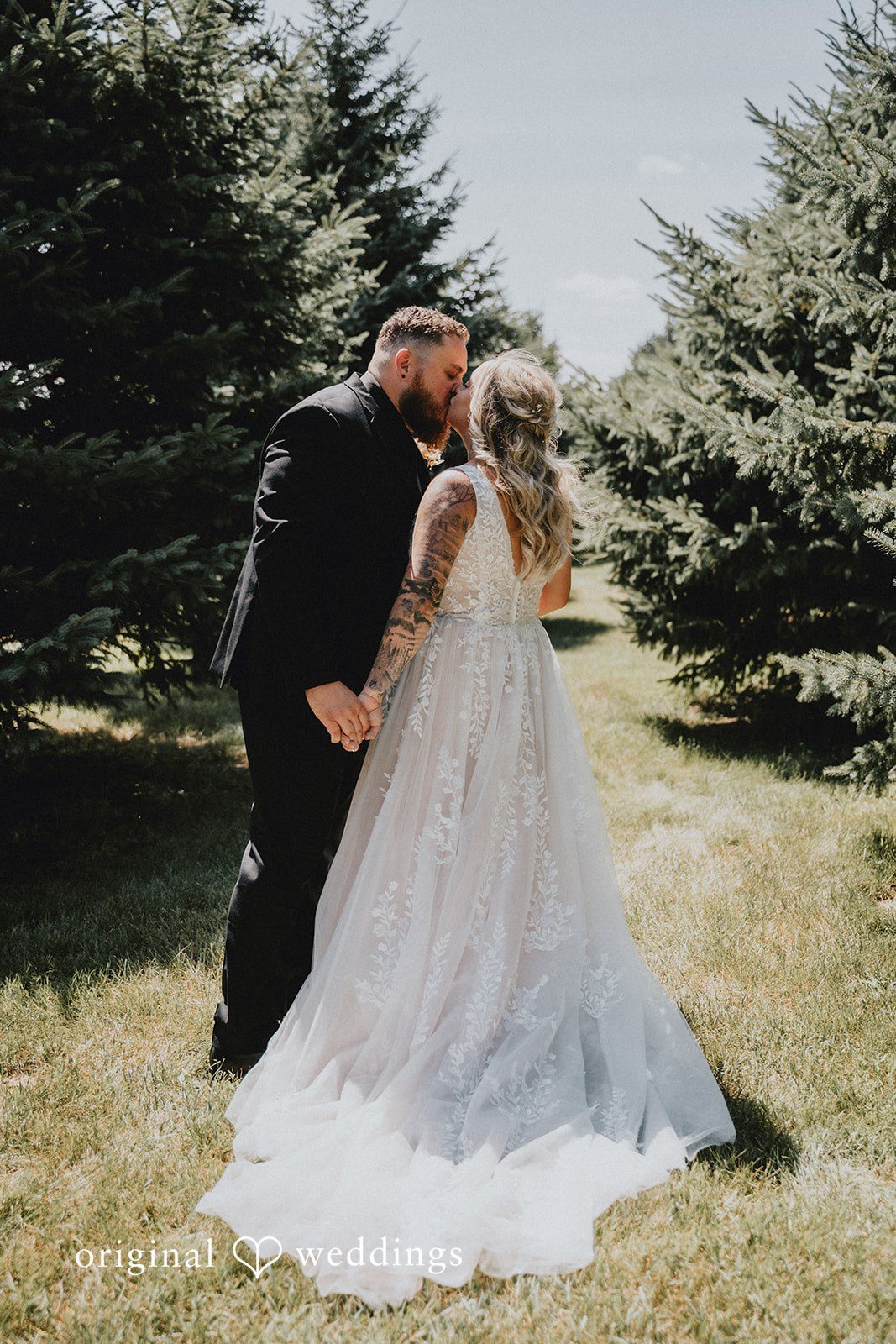 Samantha + Peyton Newlyweds sharing a kiss surrounded by evergreen pine trees.