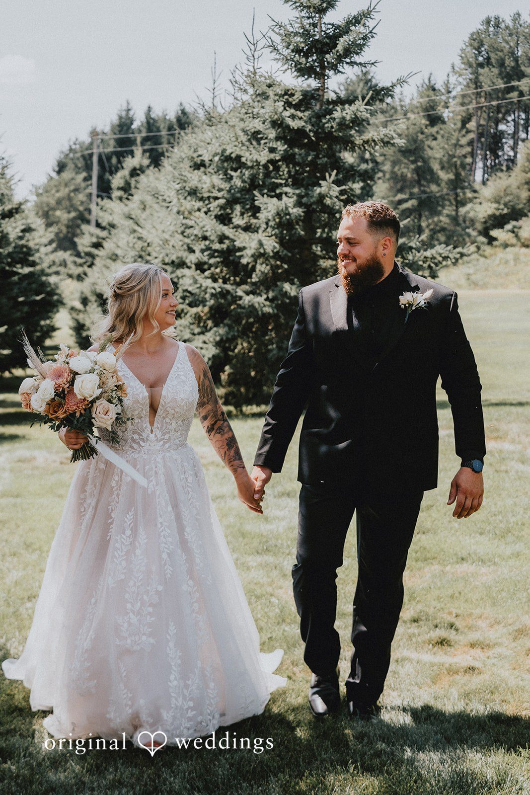 Samantha + Peyton Newlyweds holding hands while walking through a bright open field.
