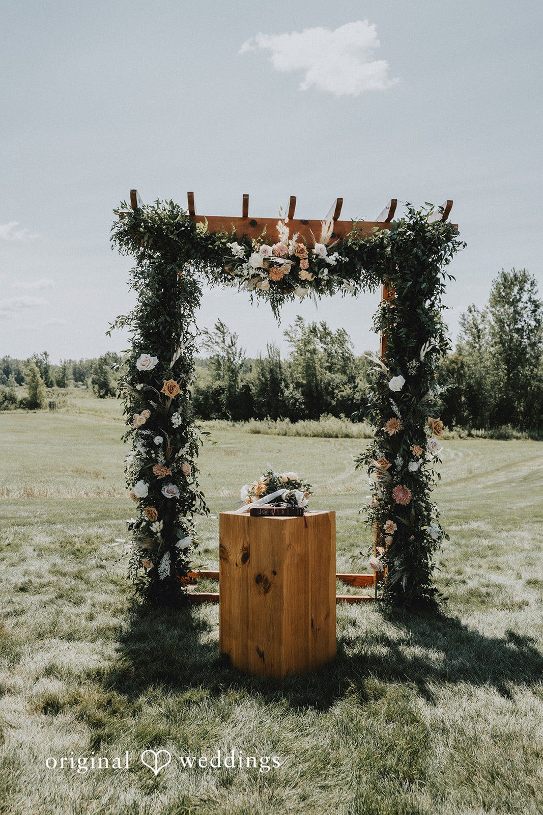 Samantha + Peyton Greenery wedding arch standing in an open field.