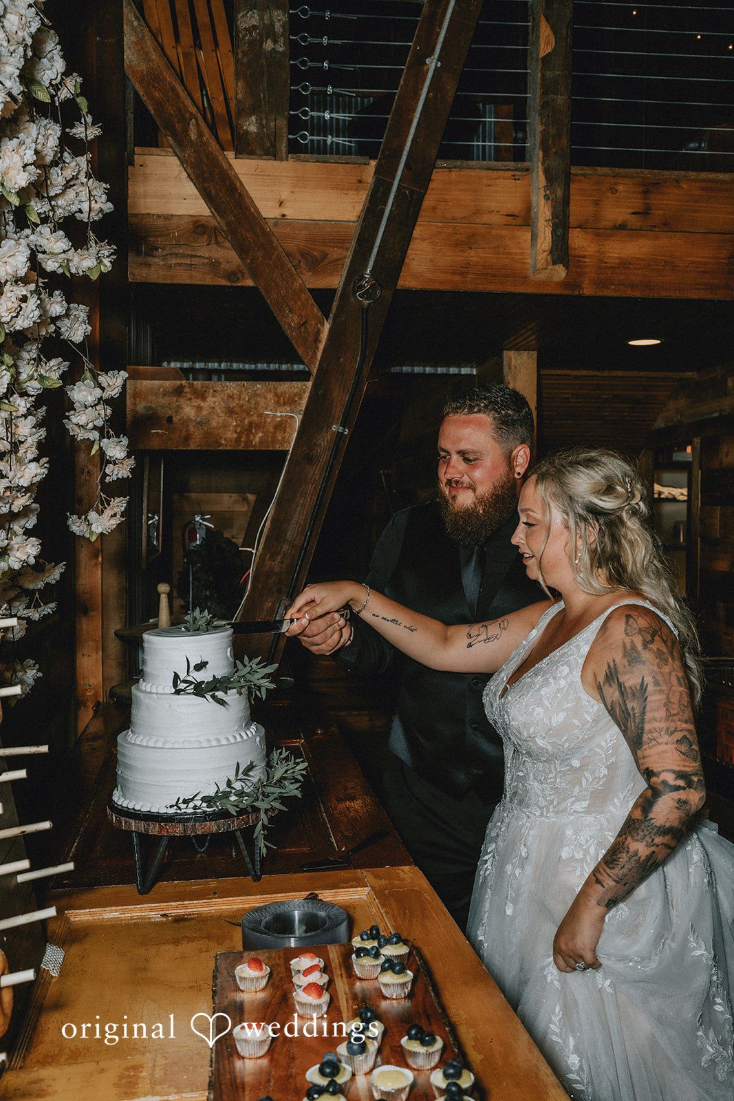Samantha + Peyton Newlyweds cutting their tiered wedding cake inside a wooden barn.