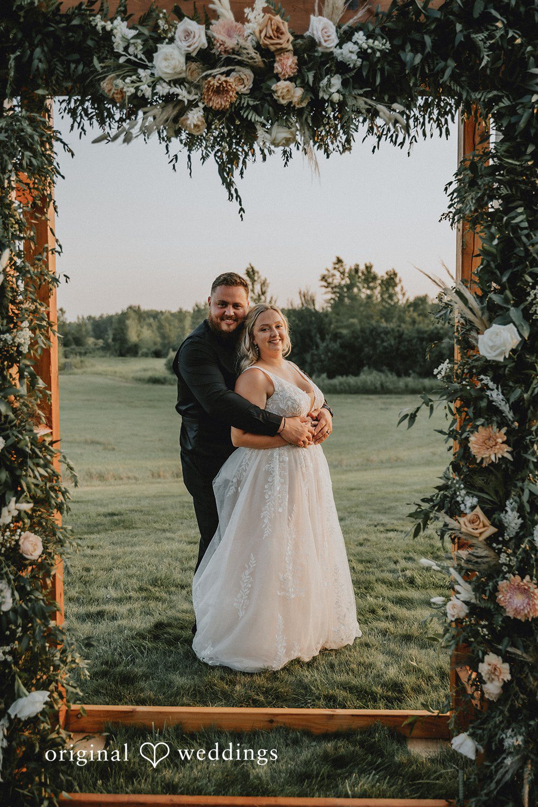 Samantha + Peyton Newlyweds posing together framed within a large floral archway.