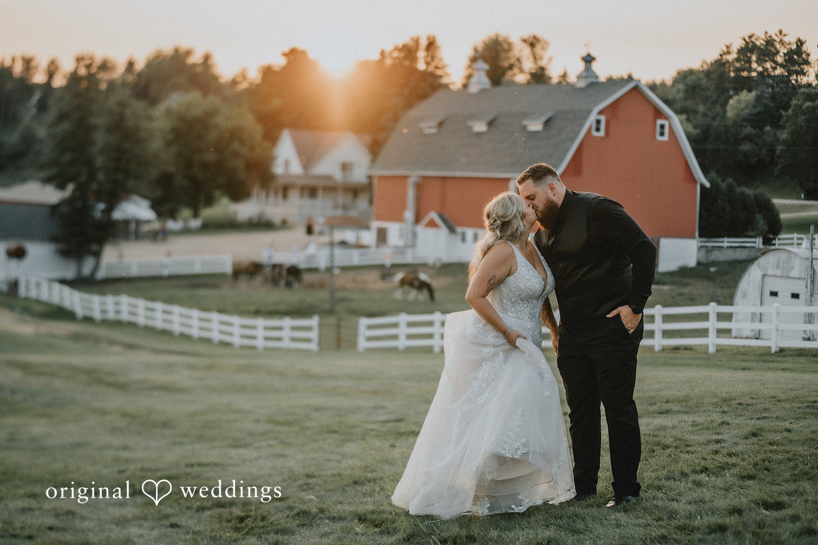 Samantha + Peyton Newlyweds sharing an embrace near a rustic red farm building.