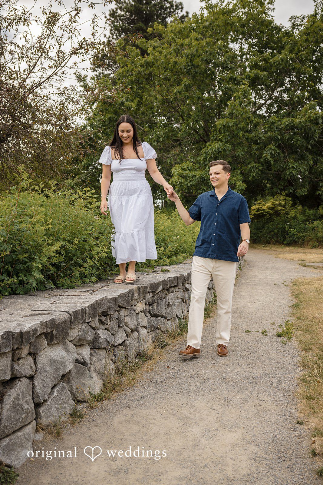 A couple walking down a set of wide stone steps surrounded by lush trees.