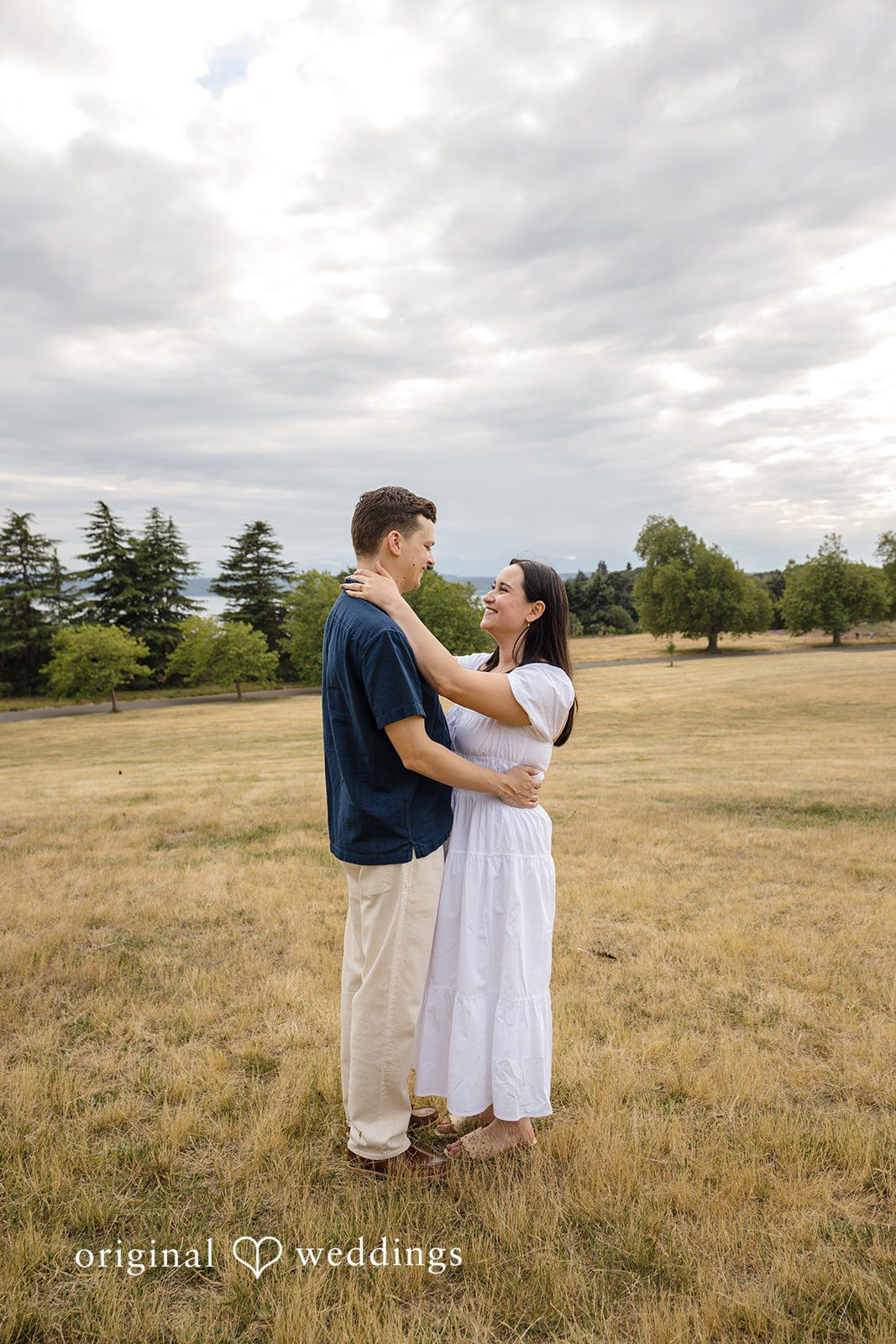 A couple embracing while standing in the middle of a vast, dry grassy field.