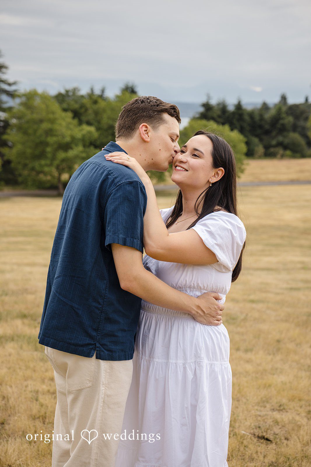 A close-up profile shot of a man hugging a woman from behind in a field.