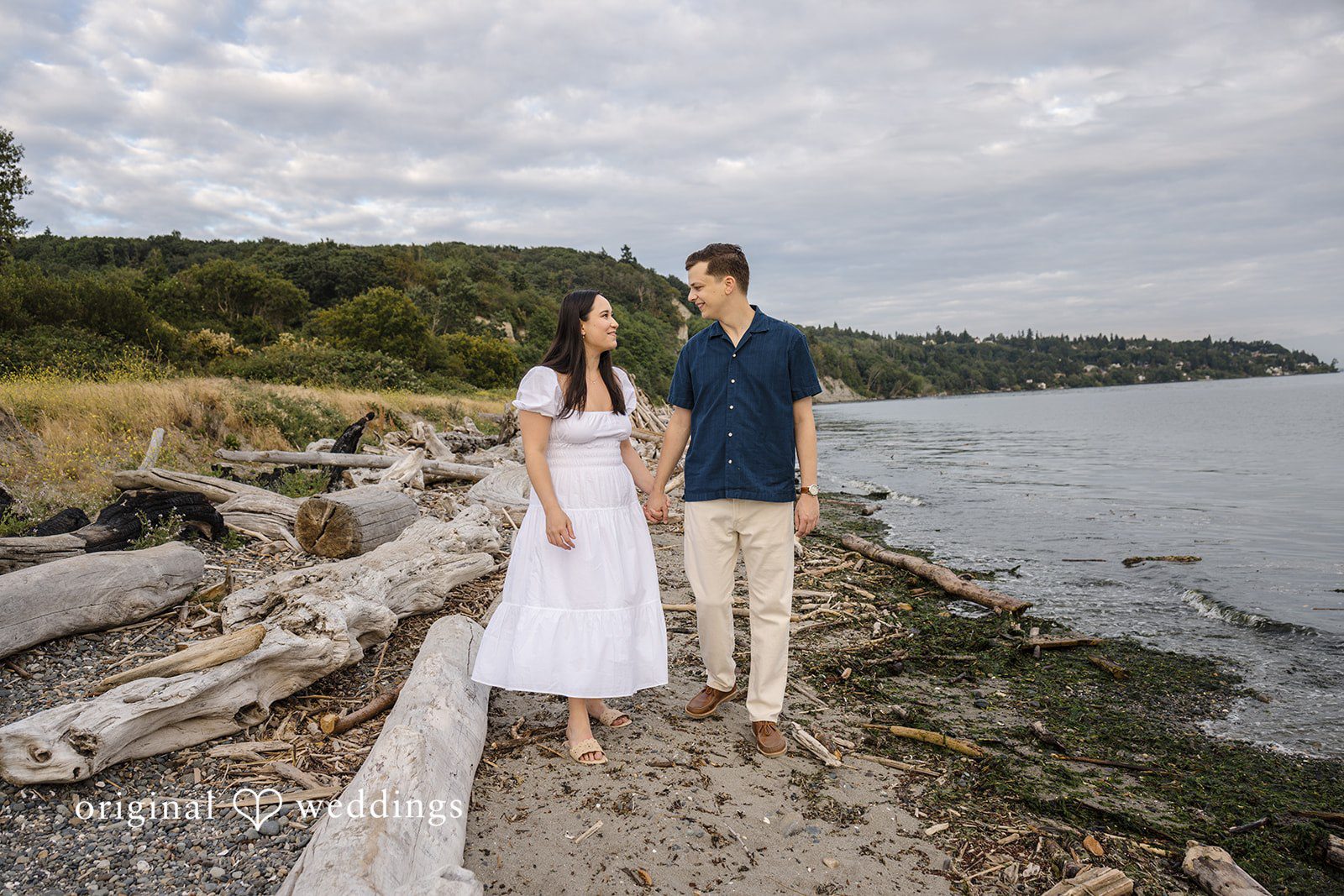 A couple standing next to a rustic wooden fence overlooking a body of water.