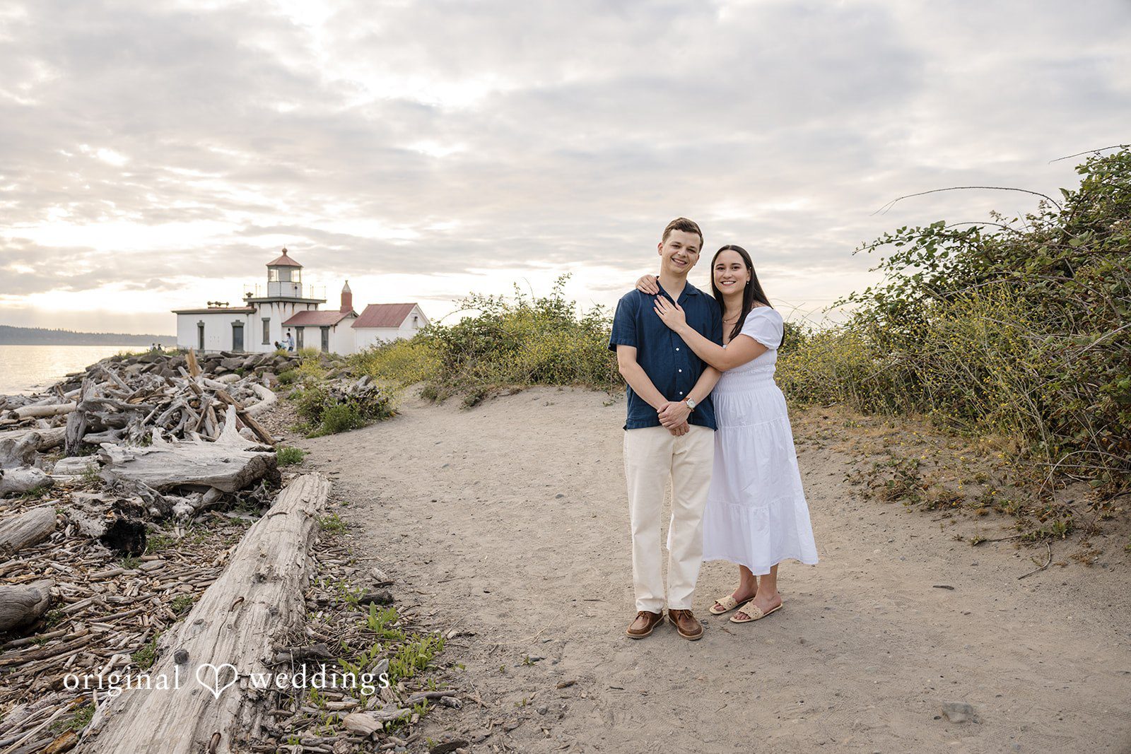 A couple standing side-by-side on a wooden boardwalk path with water in the distance.