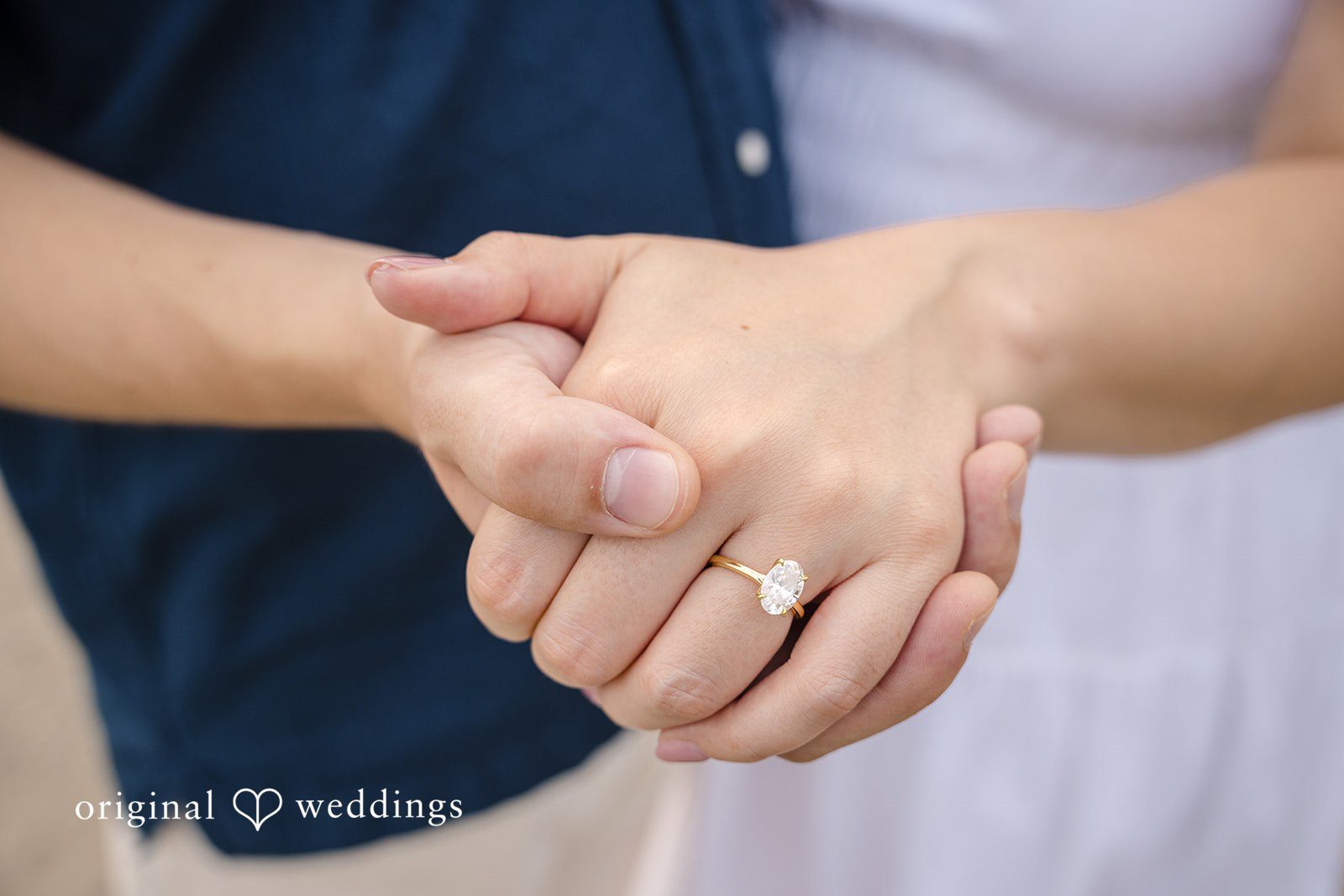 A close-up shot of a couple holding hands, highlighting a ring on the man's finger.