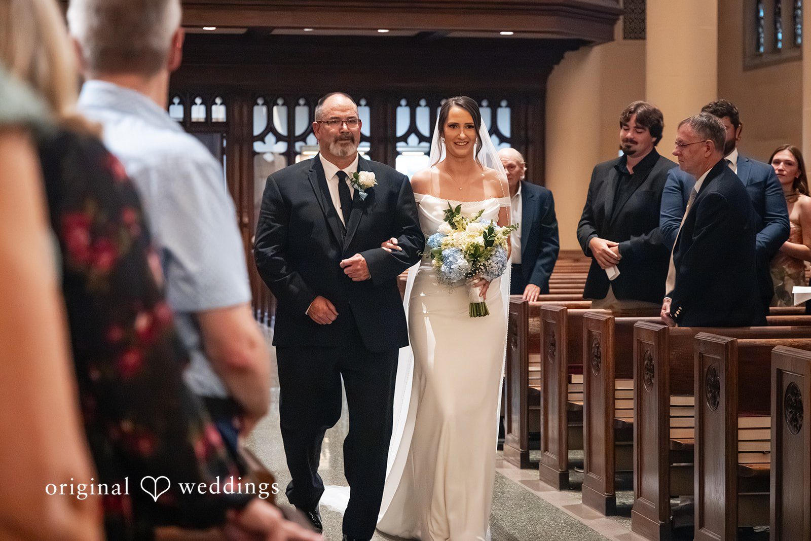 Mark + Caroline A bride walking down the church aisle accompanied by her father.