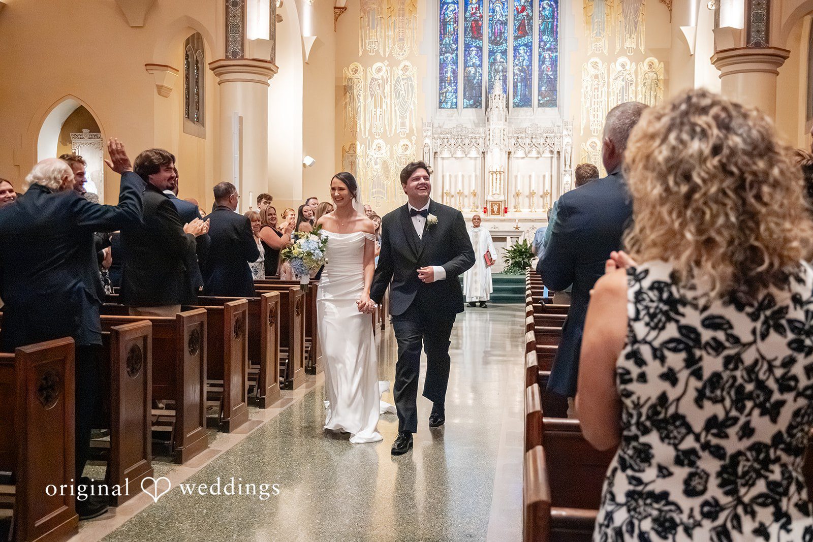Mark + Caroline The newly married couple walking back down the aisle together as guests look on.