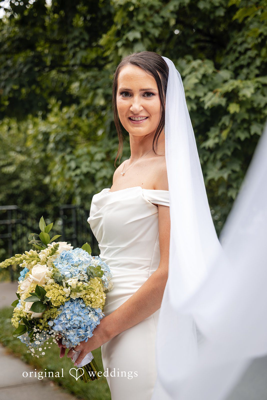 Mark + Caroline A smiling bride in a white wedding gown holding a bouquet.