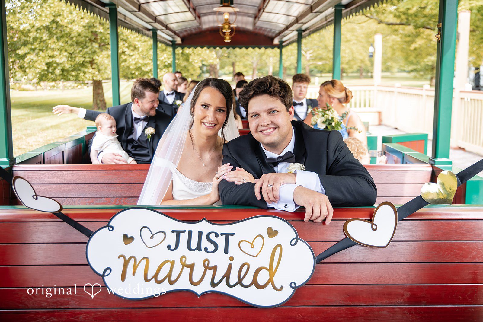 Mark + Caroline The bride and groom waving from the back of a trolley decorated with a "Just Married" sign.