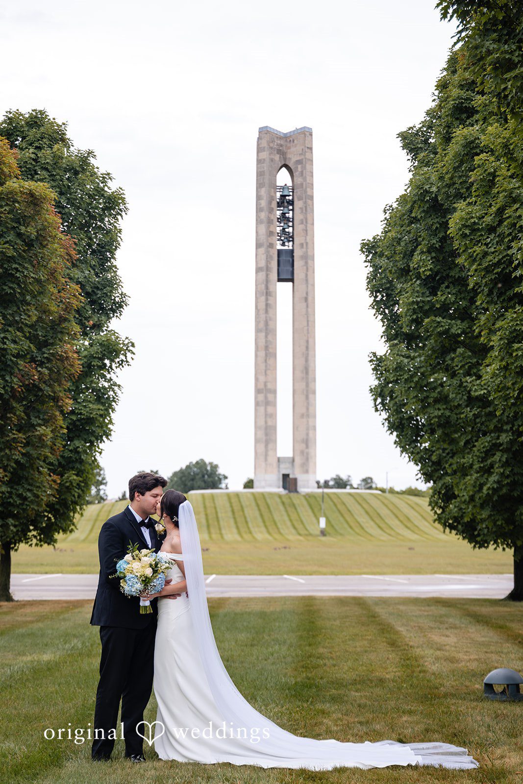 Mark + Caroline The bride and groom kissing on a lawn with a tall stone tower in the distance.